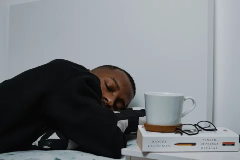 Homem descansando com livro de Daniel Kahneman e xícara ao lado, simbolizando pausa e reflexão para combater fadiga mental no trabalho.